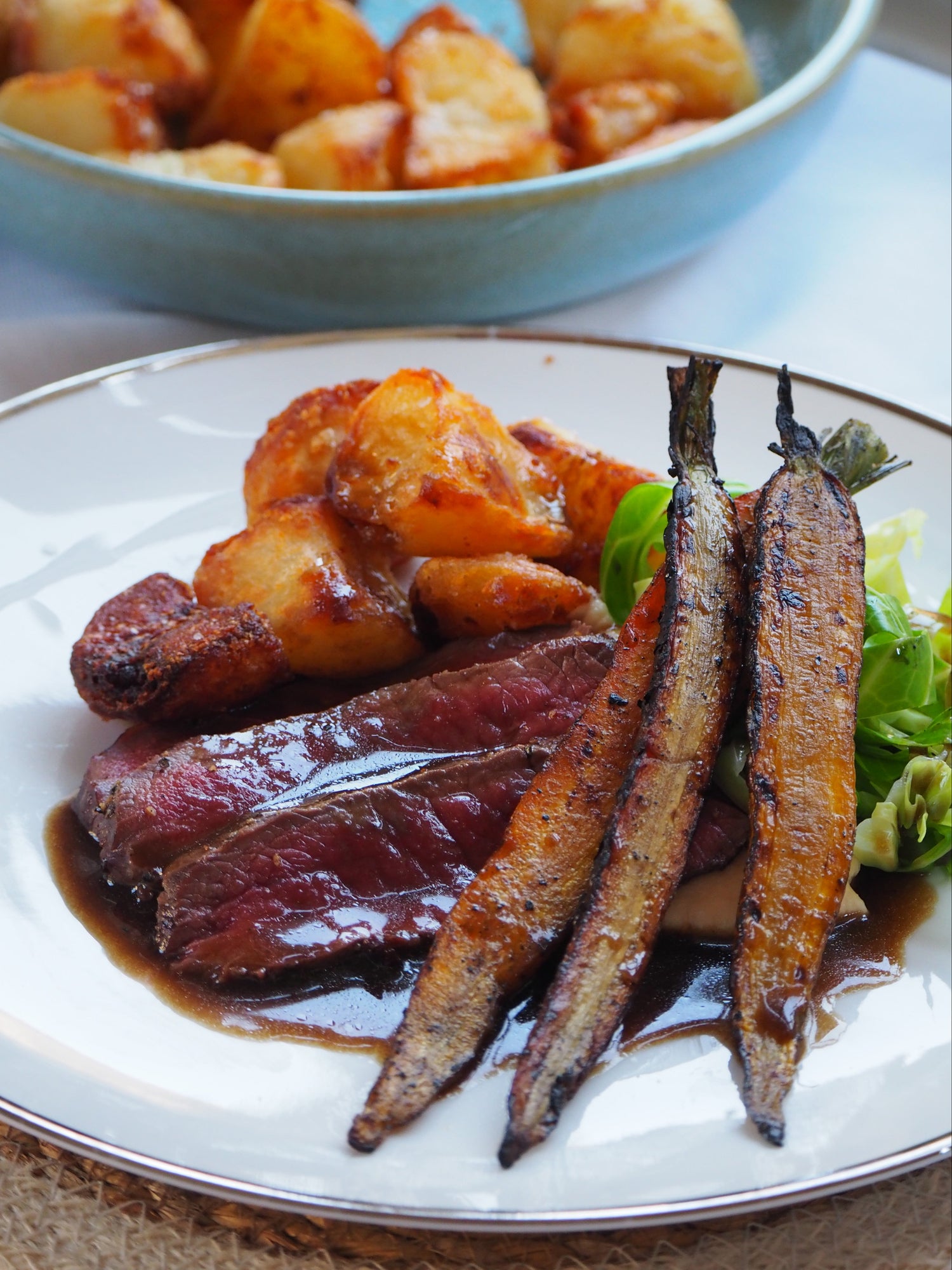 Plated dish with roasted carrots, beef, and potatoes on a white plate.